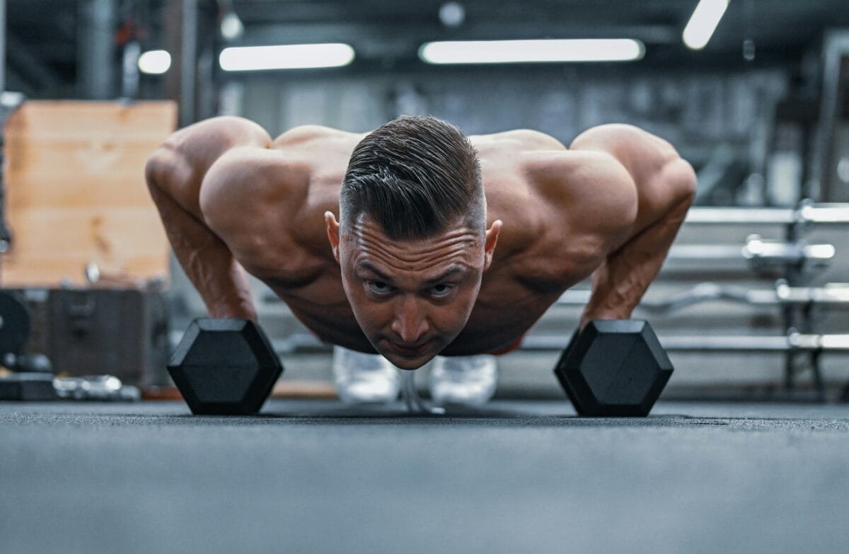 Fit man doing push-ups on hex dumbbells in a modern gym setting.