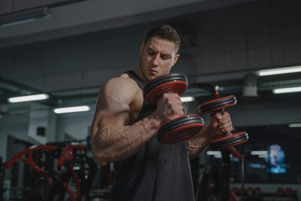 A strong man exercises with dumbbells, showcasing muscular build in a gym environment.