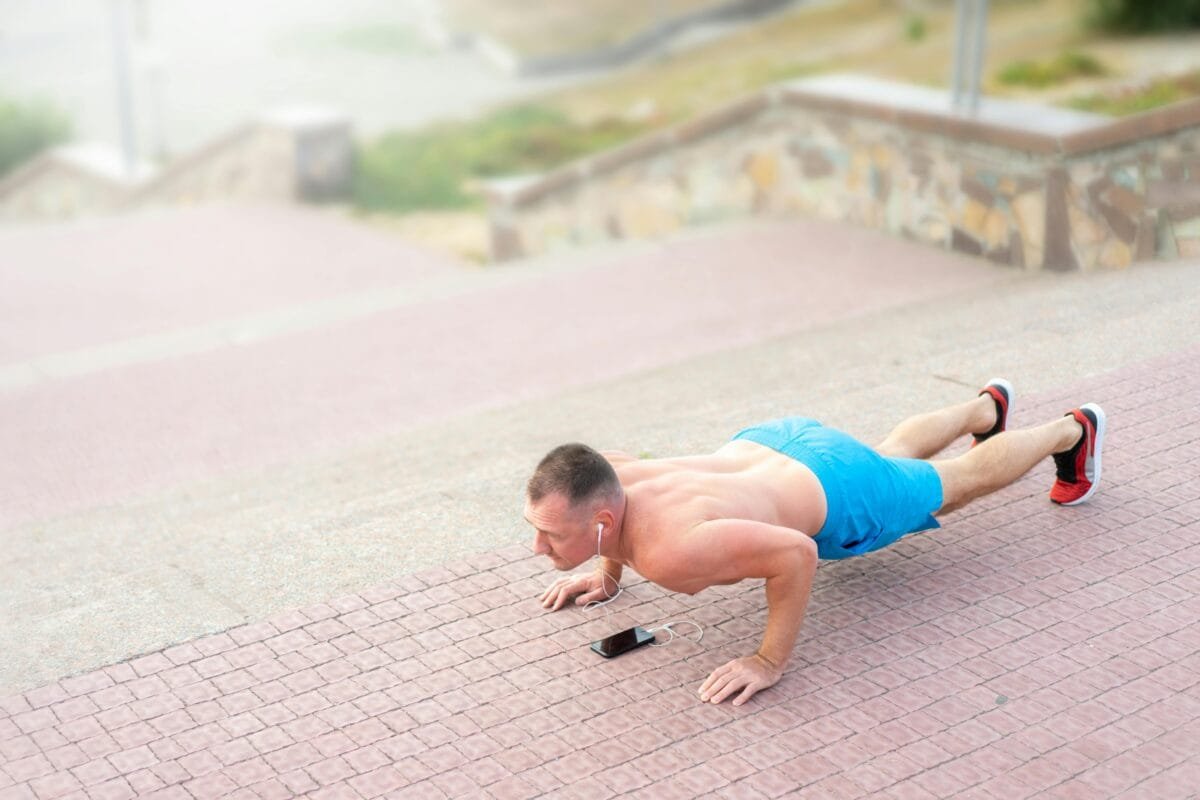 A fit man listening to music and doing push-ups outside on stairs.