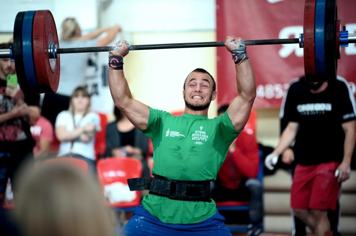 A strong athlete lifts a heavy barbell during a weightlifting competition indoors.